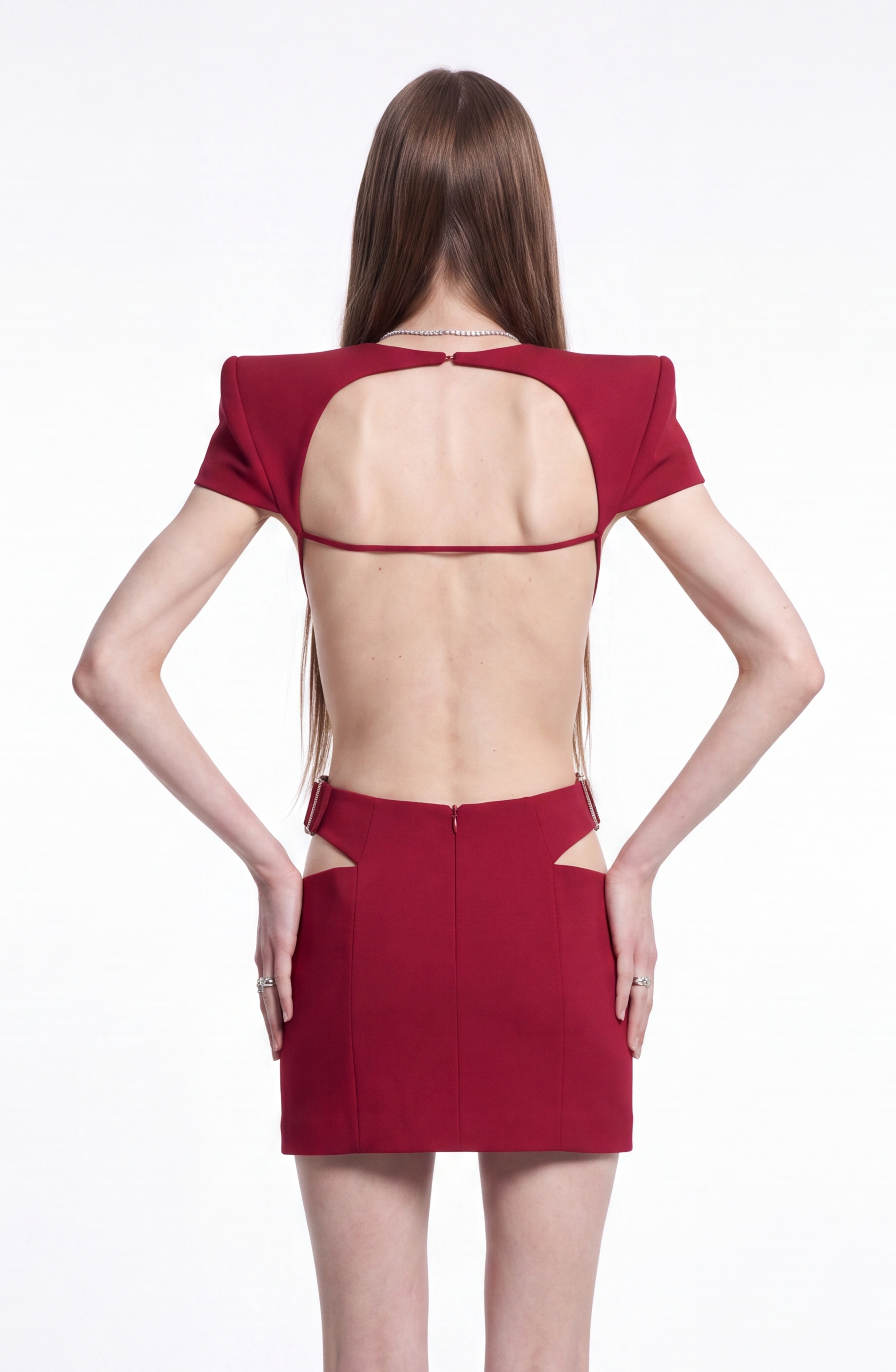 A person with long hair is wearing the LOULOU Crystal-Embellished Cutout Mini Dress, featuring padded shoulders, and is standing against a plain white background, facing away from the camera.