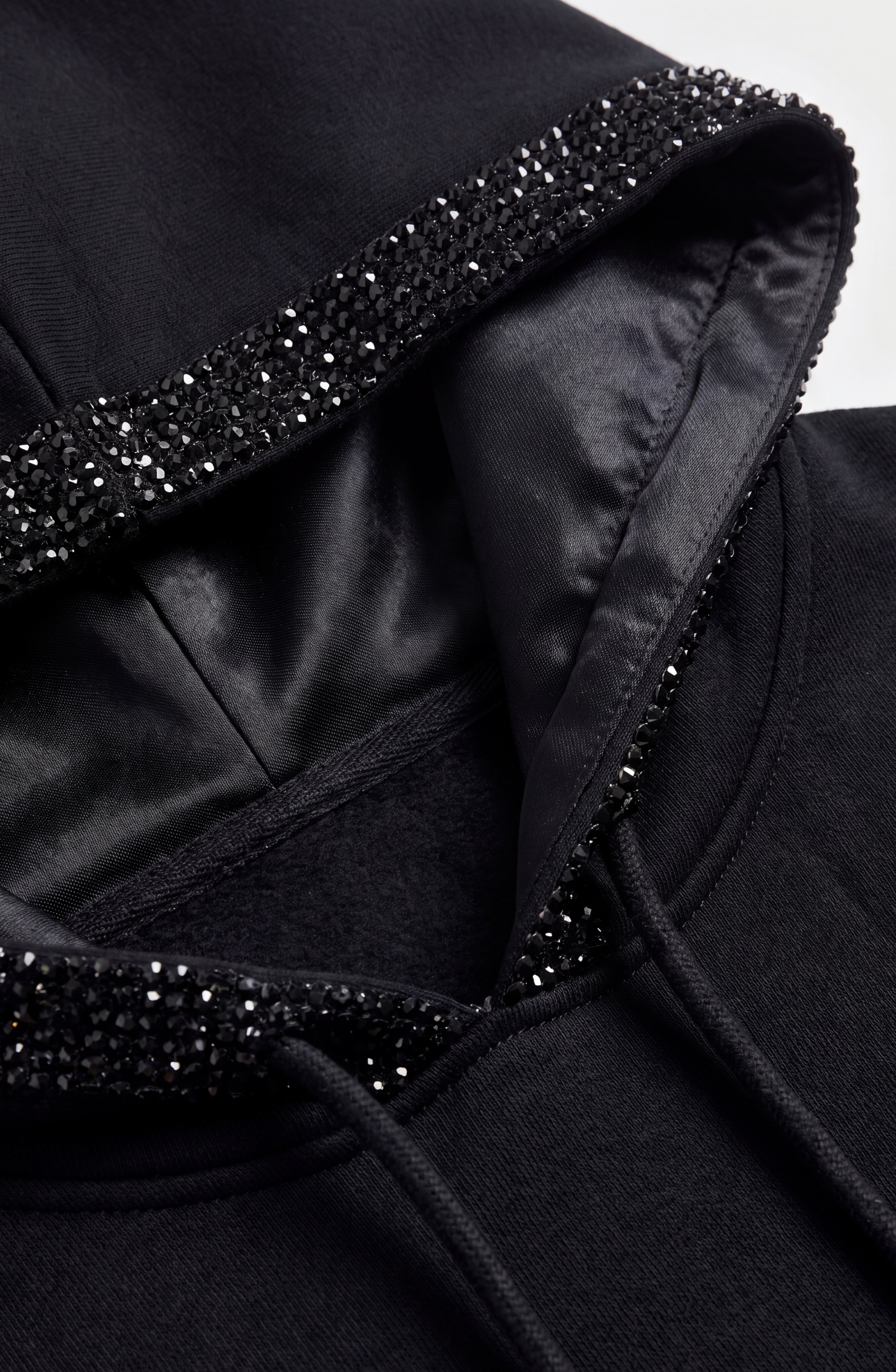 Here is the rewritten sentence using your product data: Close-up of the LOULOU Crystal Trim Asymmetrical Hoodie, an oversized style crafted from heavyweight cotton jersey, featuring a satin-like hood lining and black crystal embellishments along the edges of the hood.