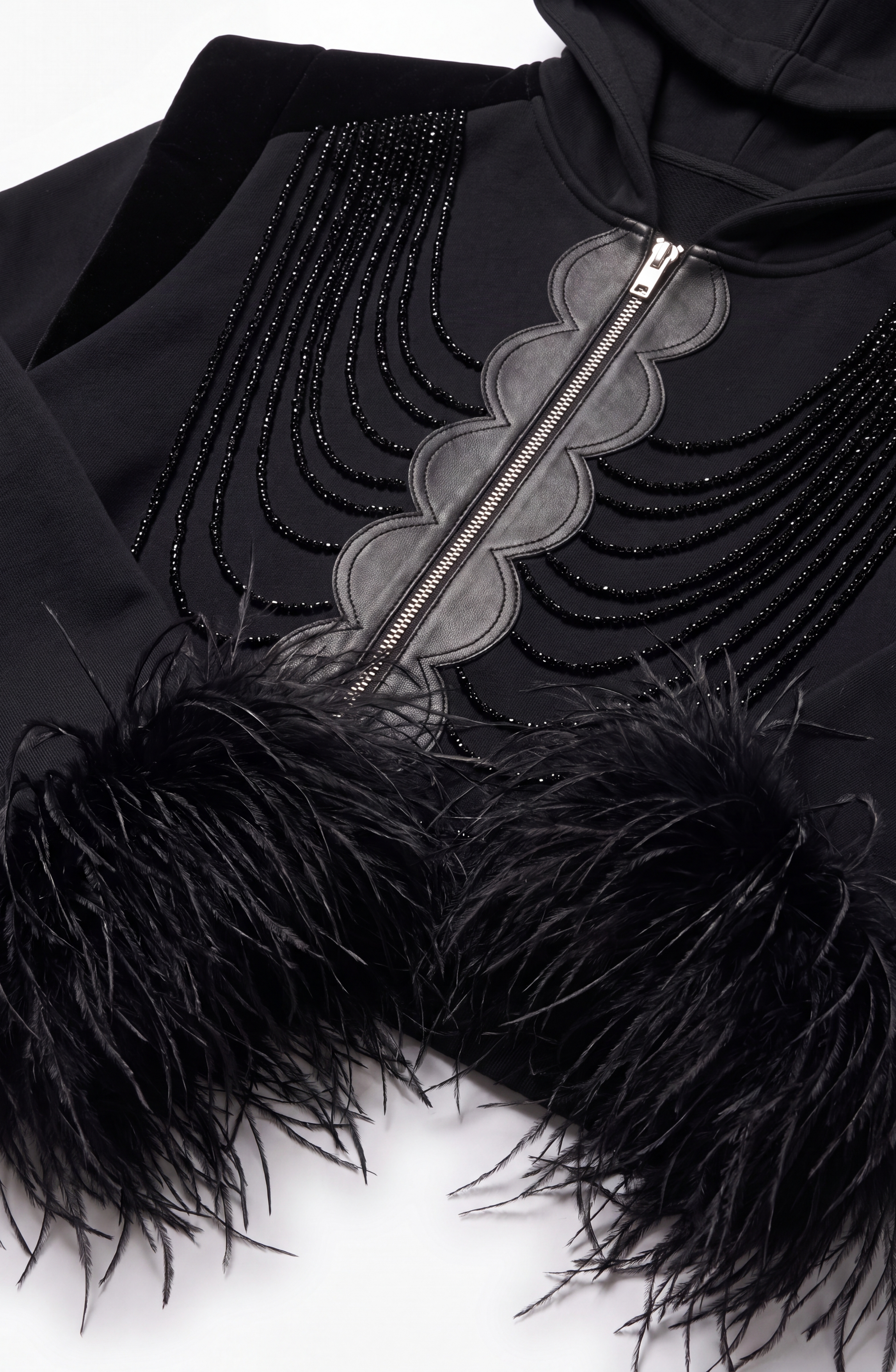 The LOULOU Embellished Feather Trim Zip Hoodie is an oversized jet black piece featuring curved bead embellishments, a central zipper, luxurious velvet accents, and statement feather-trimmed sleeve cuffs, displayed against a white background.