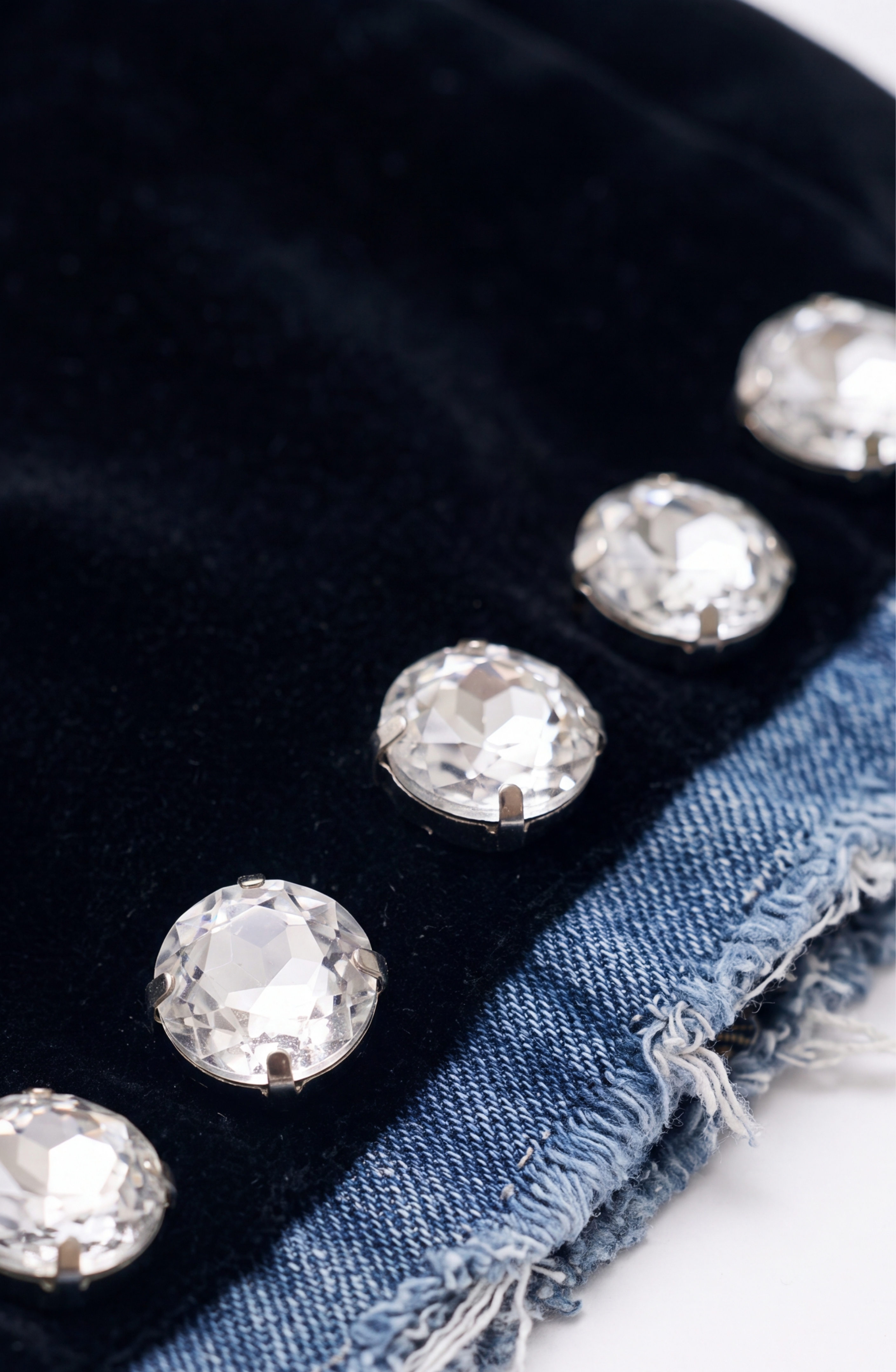 Close-up of large, faceted crystal buttons adorning the seam where plush black velvet meets frayed-edge blue denim on the LOULOU Velvet And Denim Crystal Blazer, highlighting a striking contrast reminiscent of glass crystal embellishments.