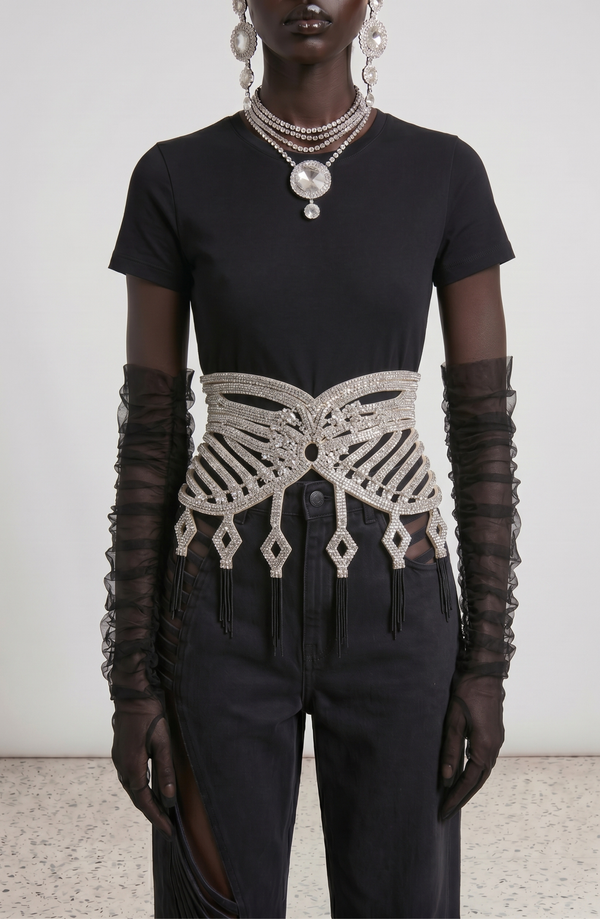 A person wearing a black t-shirt, black pants with side slits, sheer black gloves, layered silver jewelry, and the LOULOU Center Stage Belt featuring geometric patterns and sparkling glass crystals.