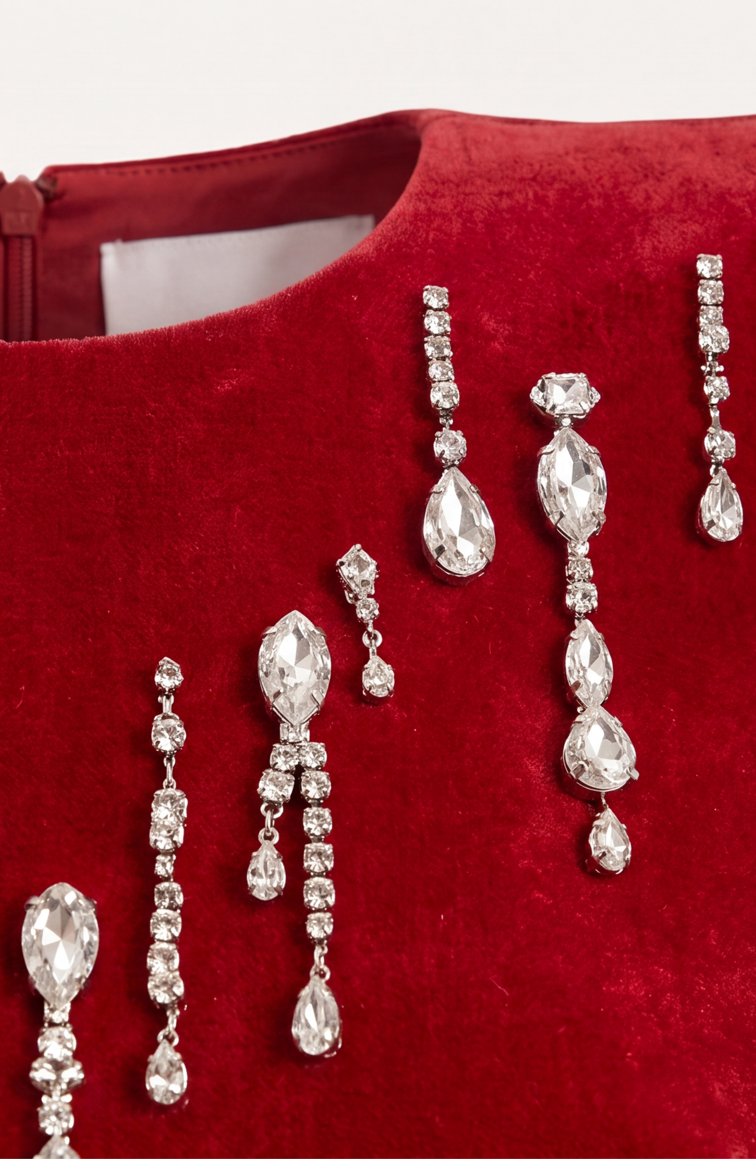 Dangling crystal earrings rest on red velvet, mirroring the glamour of the LOULOU Scarlet Velvet Mini Dress, with a zippered detail peeking from the top.