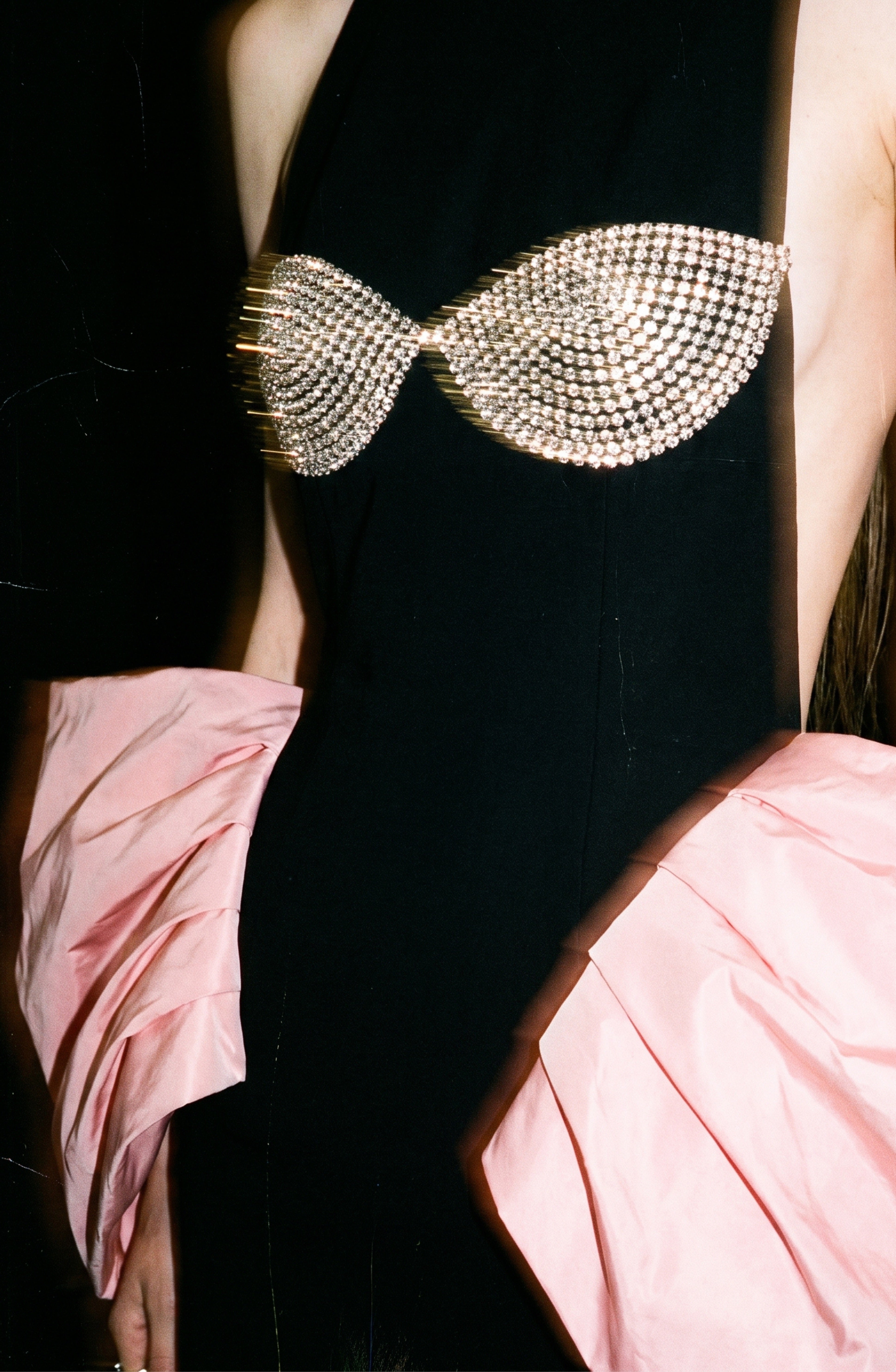 A person wearing the LOULOU Balloon Sleeve Gown, featuring a black column silhouette with a crystal-embellished bustier and oversized pink balloon sleeves. The image is cropped to show only the torso and arms.