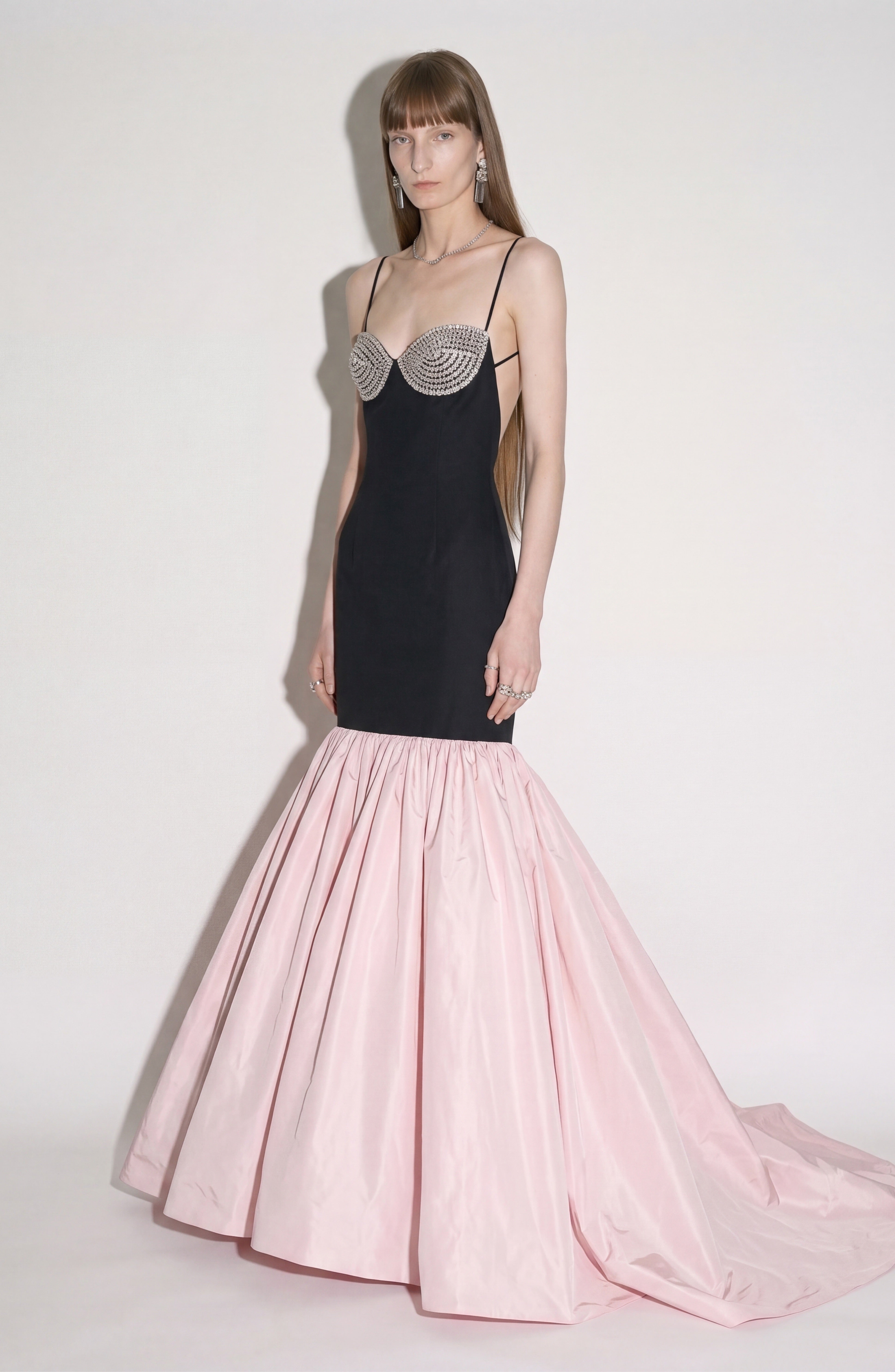 A model showcases the LOULOU Contrast Mermaid Gown, a striking black strapless evening dress with a crystal-embellished bustier and a dramatic pale pink mermaid skirt finished with a sweeping train, standing against a plain backdrop.