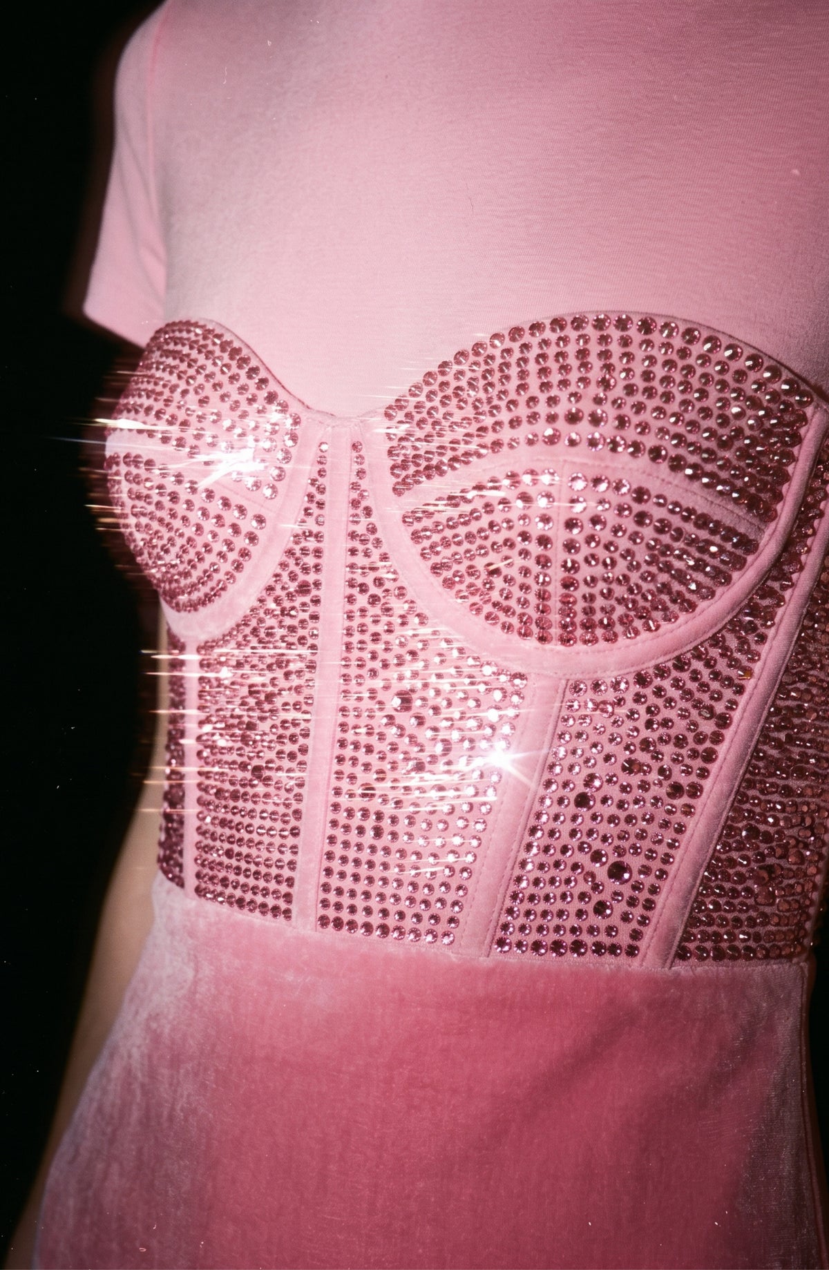 A close-up of a person wearing the LOULOU Corset Mermaid Gown in pink, showcasing its velvety fabric and crystal-embellished, corset-style bodice that glimmers under bright lighting.