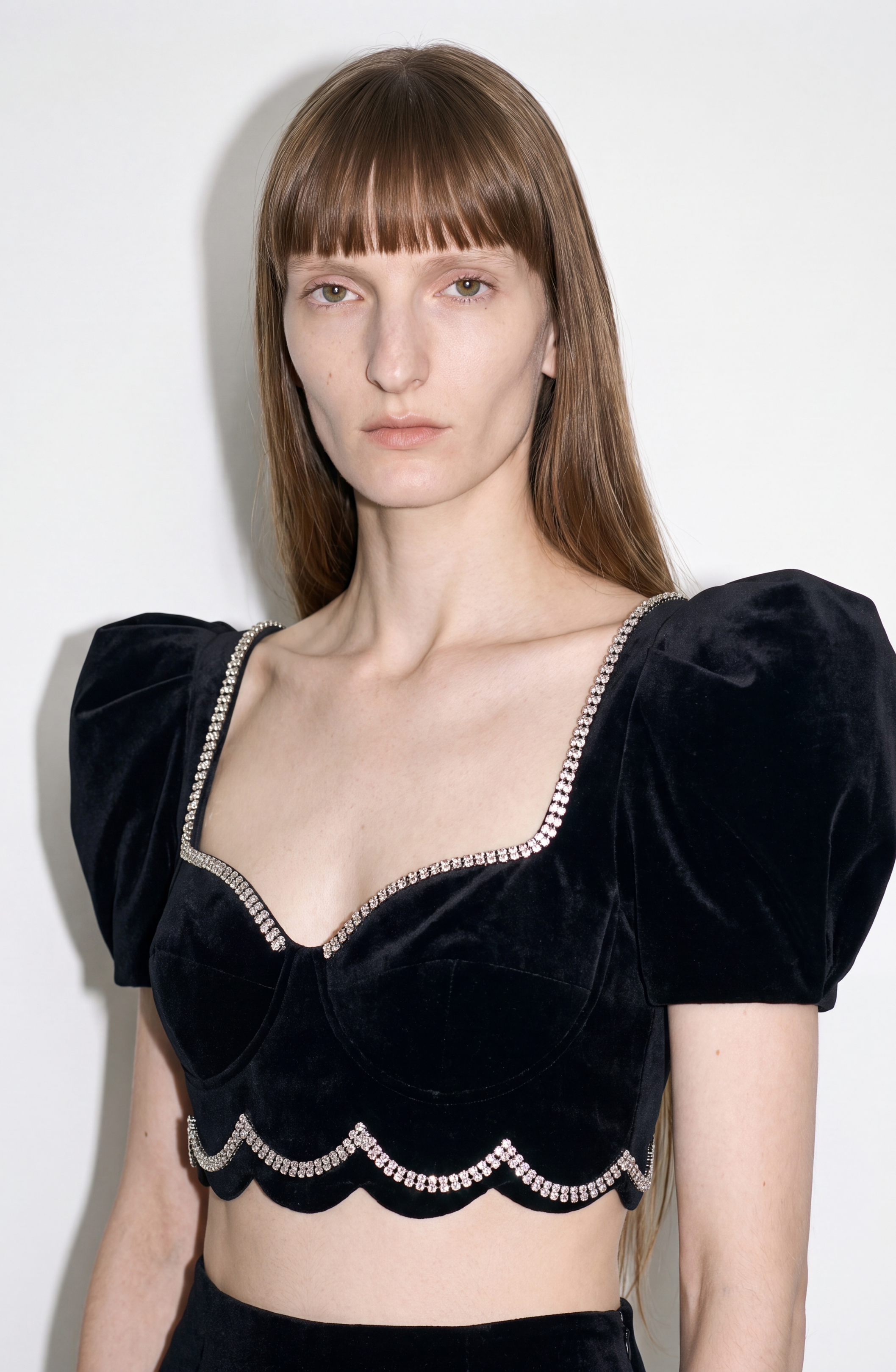 A person with long straight hair wears the LOULOU Crystal-Trim Velvet Crop Top, featuring puff sleeves and rhinestone accents, standing against a plain white background.