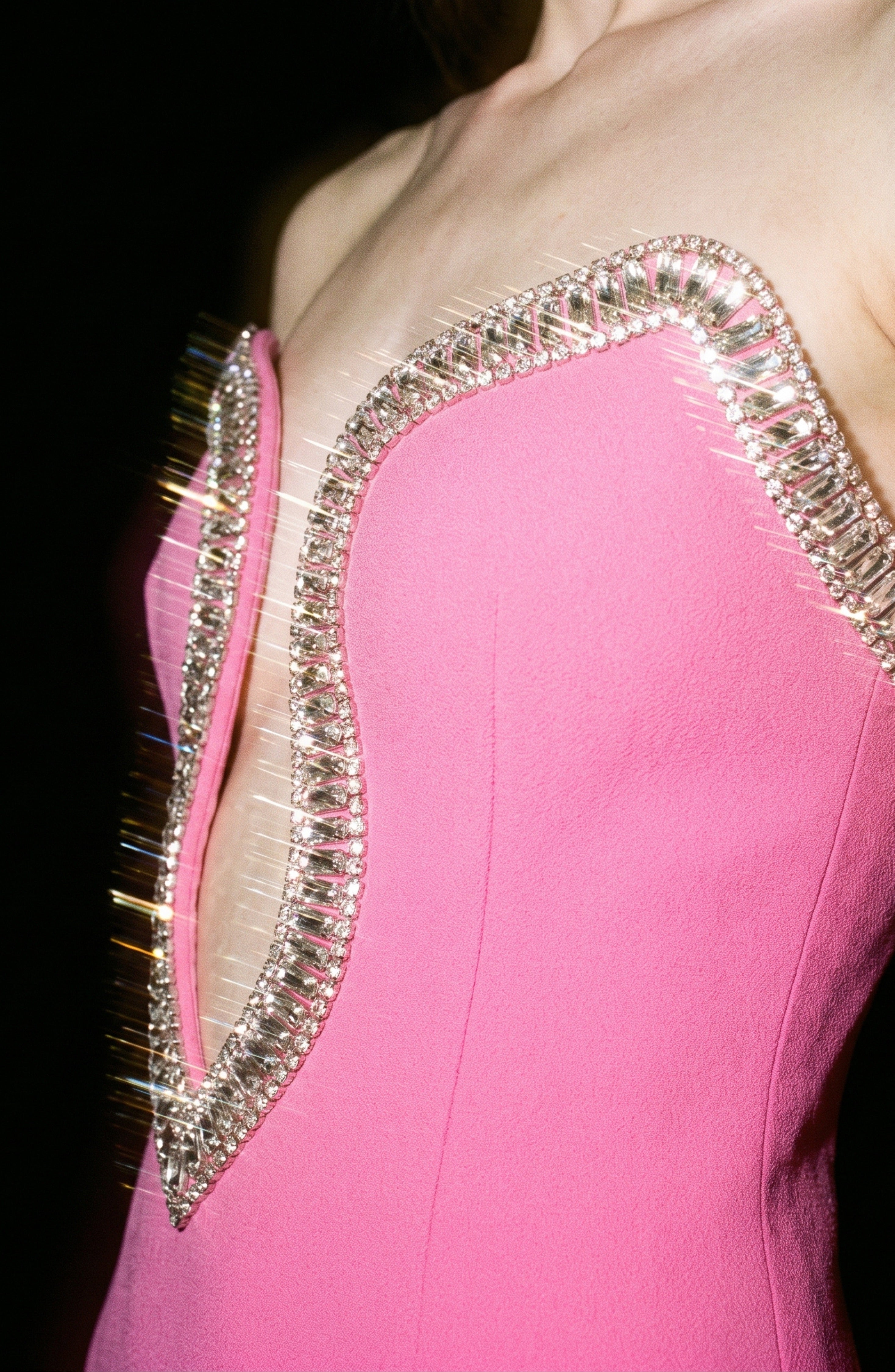 A close-up of LOULOU’s Crystal Trim Mini Dress in pink crepe, showcasing its strapless silhouette and deep V neckline embellished with sparkling silver and glass crystal details along the edge.