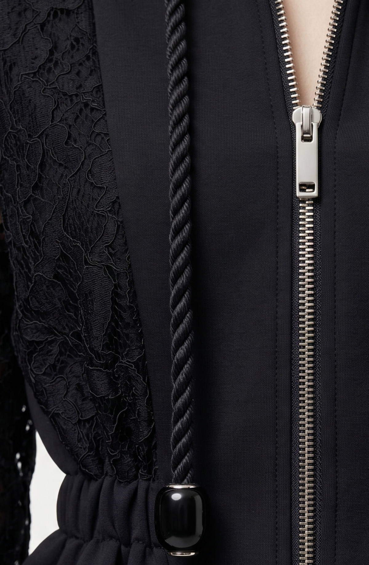 Close-up of LOULOU’s After Hours Bomber in black cotton, featuring a metallic zipper, thick twisted drawstring with glass beads, and a lace floral pattern on one side. Part of the wearer’s neck and chest is visible at the top right.