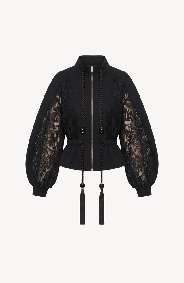 The After Hours Bomber by LOULOU is a black cotton jacket with sheer floral-lace sleeves, a cinched waist, and long tasseled drawstrings at the collar.