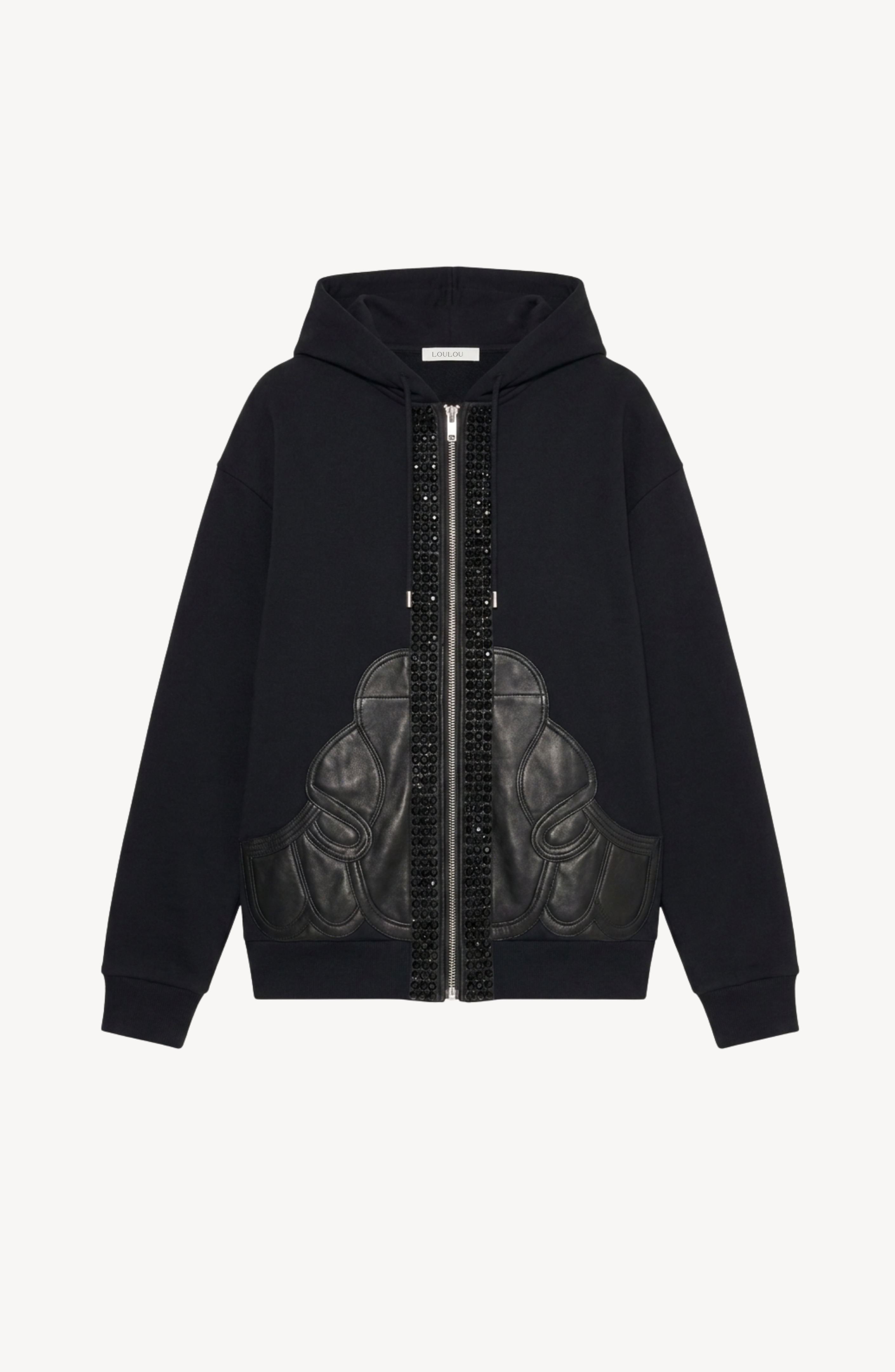 The LOULOU Embellished Leather Panel Zip Hoodie features two glossy black vertical strips flanking the zipper and distinctive leather appliqué panels across the lower front. This striking jet black zip-up hoodie is showcased against a plain white background.