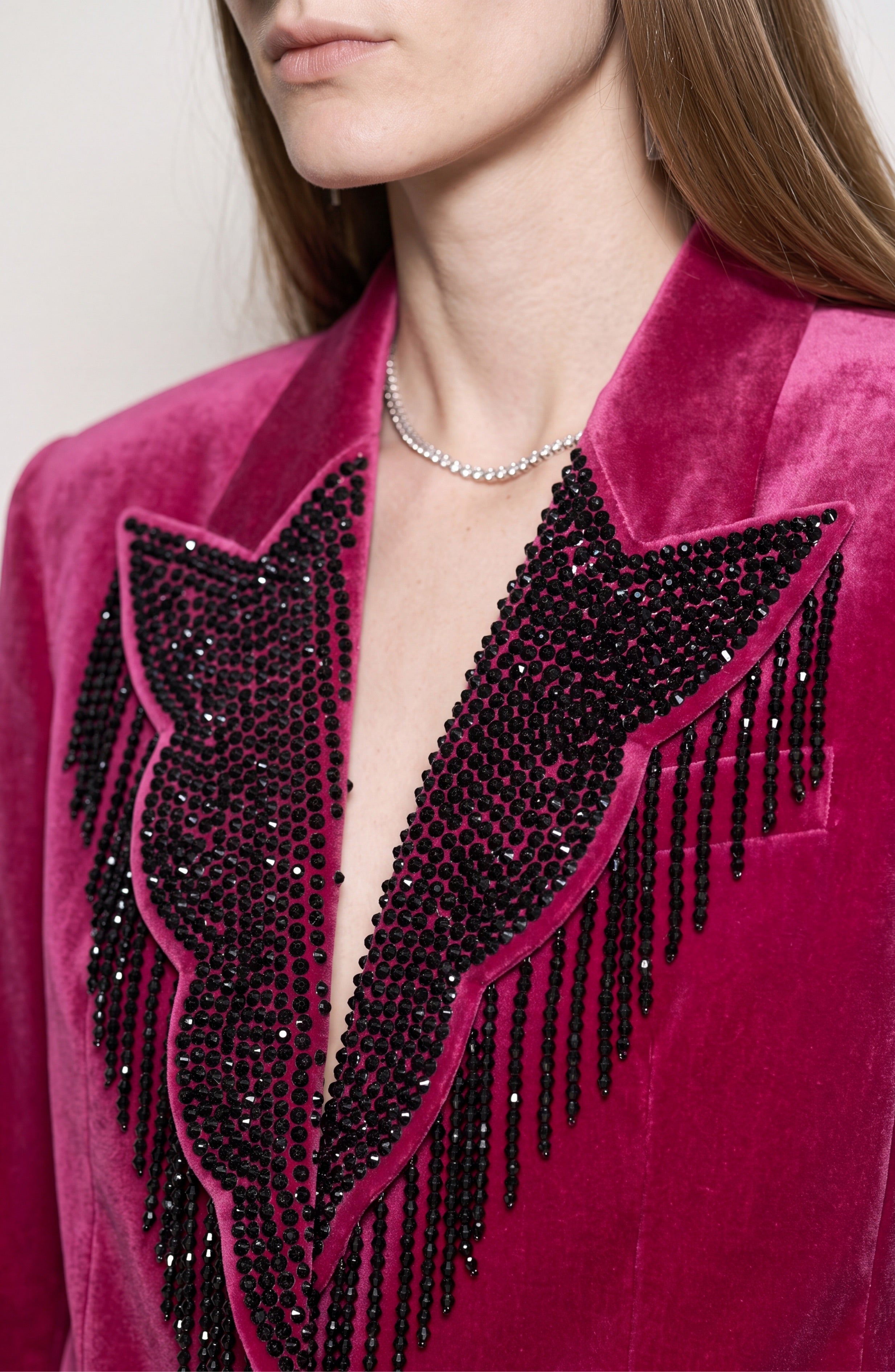 A person with long brown hair wears the LOULOU Fuchsia Velvet Blazer, featuring black beaded fringe on the lapels, paired with a delicate silver necklace. Their face is partially out of frame.