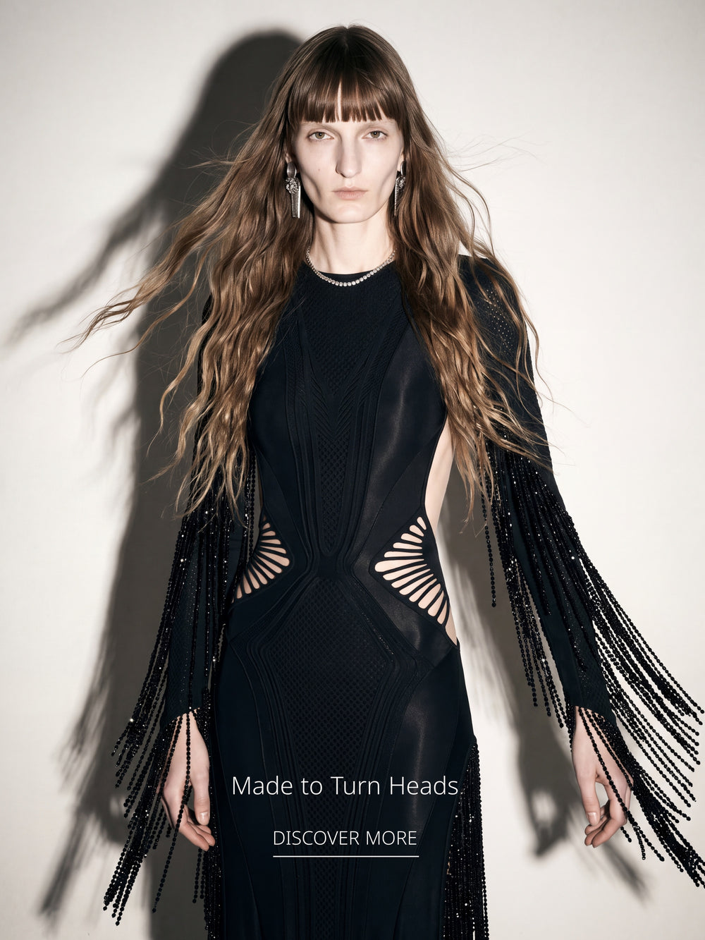 Model wearing a black sculptural cutout dress with embellished fringe sleeves from the LOULOU collection.